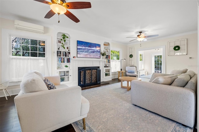 living room featuring a wall mounted air conditioner, built in shelves, ceiling fan, and wood-type flooring