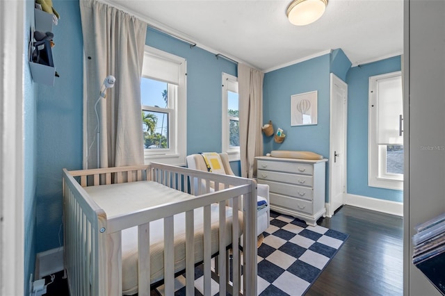 bedroom featuring dark hardwood / wood-style flooring, a nursery area, and ornamental molding