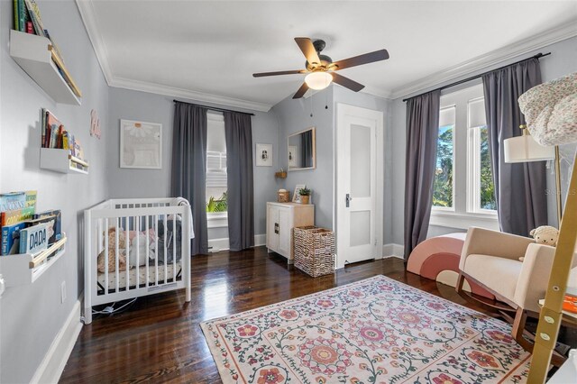 bedroom featuring ceiling fan, a crib, crown molding, and dark wood-type flooring