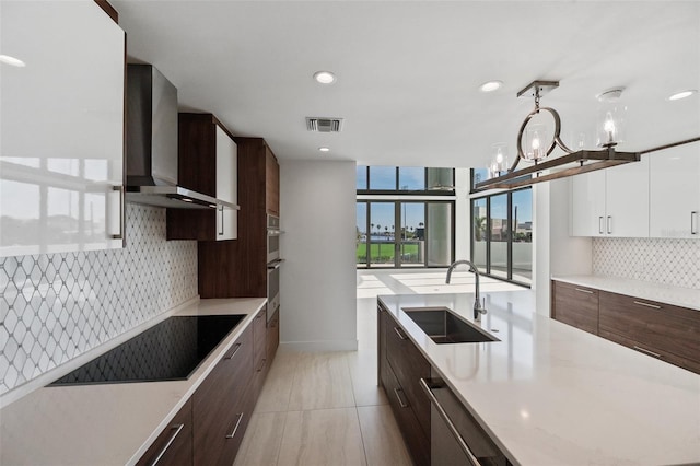 kitchen featuring sink, wall chimney range hood, decorative light fixtures, dishwasher, and white cabinets