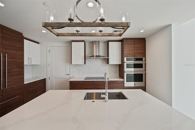 kitchen featuring tasteful backsplash, stainless steel double oven, sink, wall chimney range hood, and white cabinets