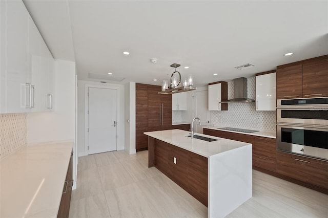 kitchen with sink, wall chimney range hood, pendant lighting, black electric cooktop, and white cabinets