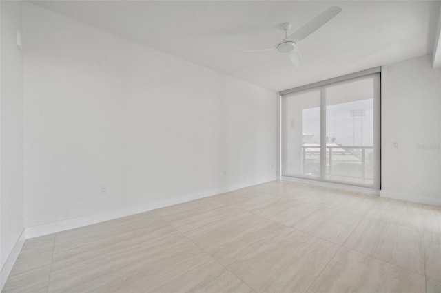 tiled empty room featuring ceiling fan and a wall of windows