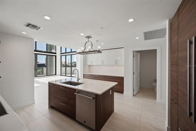 kitchen featuring decorative backsplash, sink, decorative light fixtures, a center island with sink, and white cabinetry