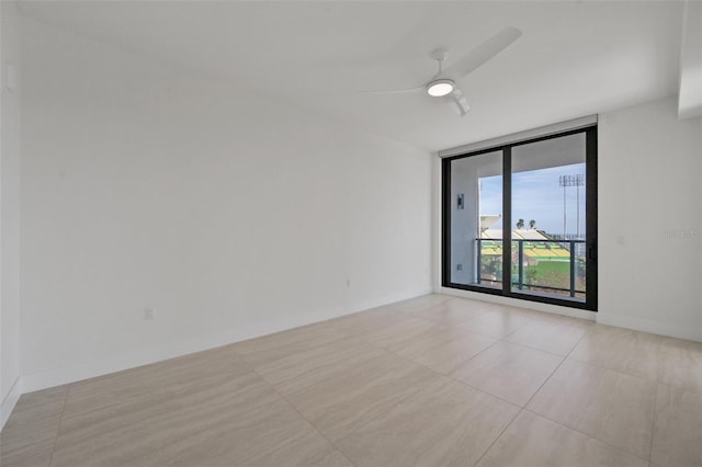 tiled spare room featuring ceiling fan and a wall of windows