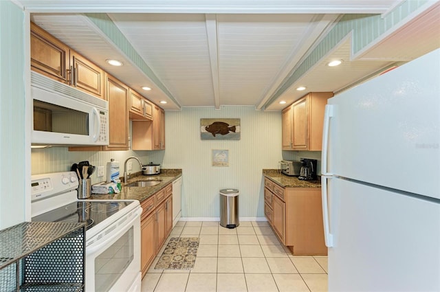 kitchen with white appliances, dark stone counters, sink, light tile patterned floors, and beamed ceiling