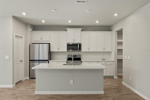 kitchen with sink, a kitchen island with sink, stainless steel appliances, light hardwood / wood-style floors, and white cabinets