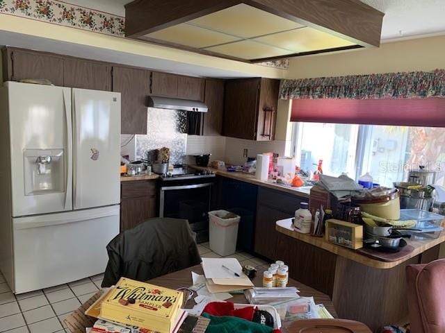 kitchen with stainless steel electric range oven, white fridge with ice dispenser, kitchen peninsula, light tile patterned flooring, and exhaust hood