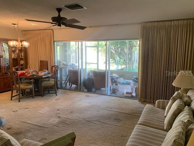 carpeted living room featuring ceiling fan with notable chandelier