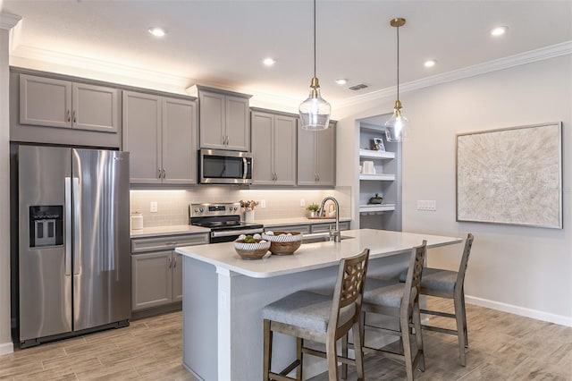 kitchen featuring hanging light fixtures, gray cabinets, ornamental molding, an island with sink, and stainless steel appliances