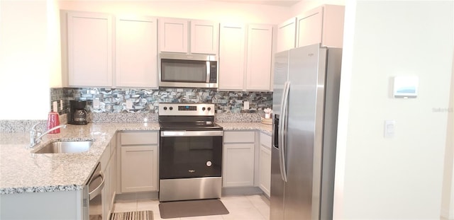 kitchen with sink, decorative backsplash, light tile patterned floors, light stone counters, and stainless steel appliances