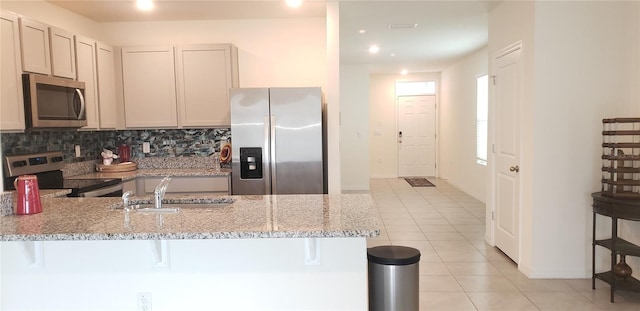 kitchen featuring kitchen peninsula, appliances with stainless steel finishes, light stone counters, a breakfast bar, and sink