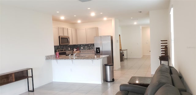 kitchen with light stone counters, a kitchen bar, decorative backsplash, light tile patterned flooring, and appliances with stainless steel finishes