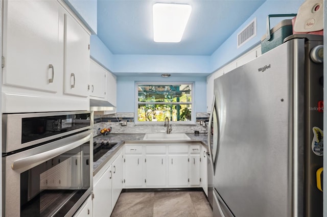 kitchen with sink, appliances with stainless steel finishes, white cabinetry, light tile patterned flooring, and decorative backsplash