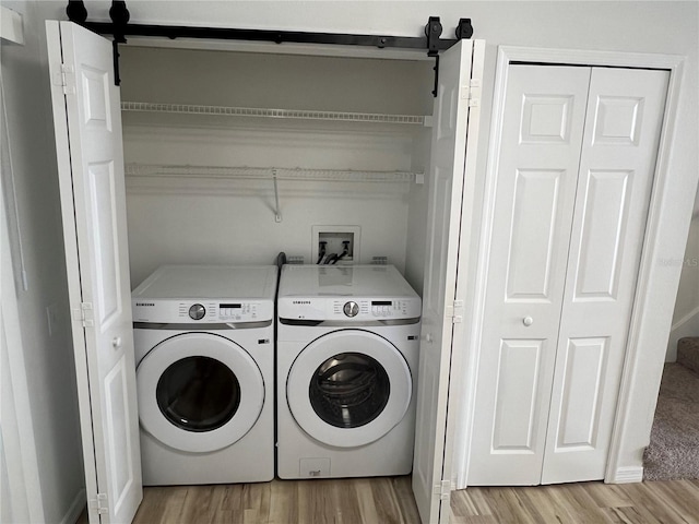 laundry room featuring a barn door, independent washer and dryer, and light hardwood / wood-style flooring