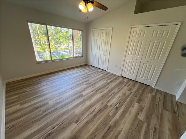 unfurnished bedroom featuring ceiling fan, lofted ceiling, light hardwood / wood-style flooring, and two closets