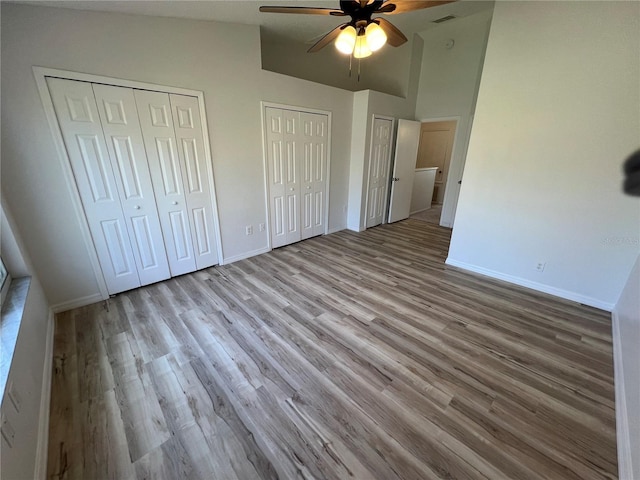 unfurnished bedroom with light hardwood / wood-style flooring, vaulted ceiling, ceiling fan, and multiple closets