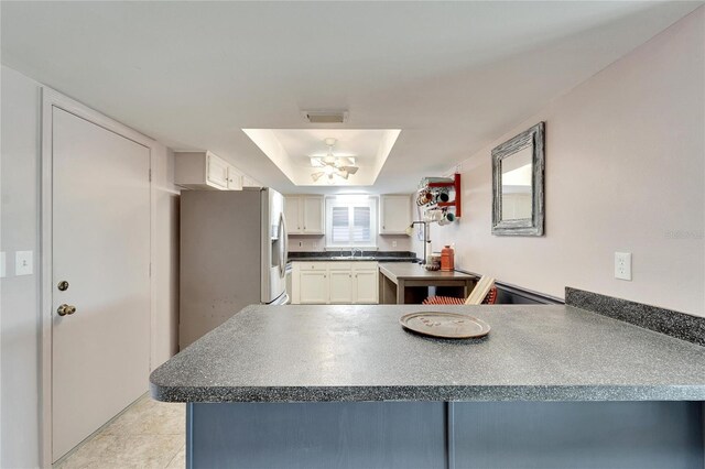 kitchen featuring stainless steel refrigerator with ice dispenser, sink, white cabinetry, a tray ceiling, and kitchen peninsula