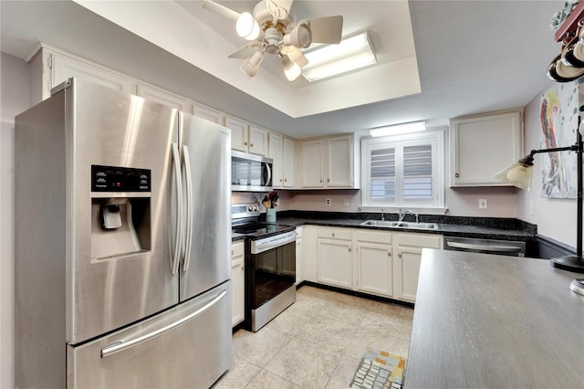 kitchen with sink, ceiling fan, appliances with stainless steel finishes, white cabinets, and a raised ceiling