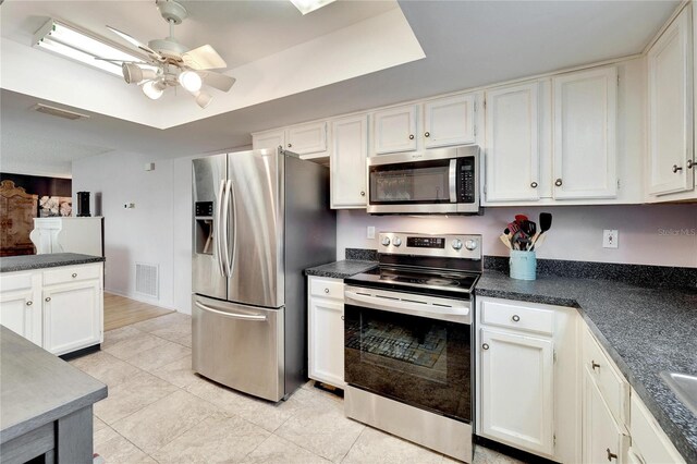 kitchen featuring light tile patterned floors, ceiling fan, white cabinetry, stainless steel appliances, and a tray ceiling