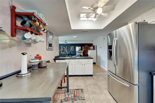 kitchen featuring light tile patterned floors, ceiling fan, stainless steel refrigerator with ice dispenser, a tray ceiling, and white cabinets