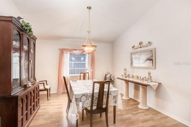 dining area with vaulted ceiling, an inviting chandelier, and light hardwood / wood-style flooring