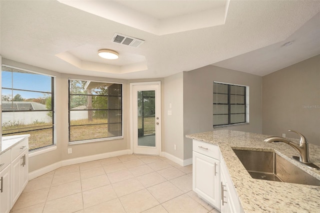 kitchen with light stone countertops, a tray ceiling, sink, light tile patterned floors, and white cabinets