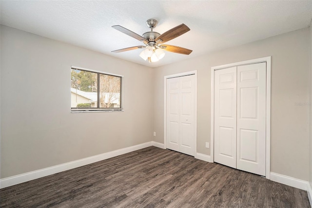 unfurnished bedroom featuring ceiling fan, dark hardwood / wood-style flooring, a textured ceiling, and multiple closets