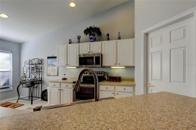 kitchen with white cabinets, appliances with stainless steel finishes, and lofted ceiling