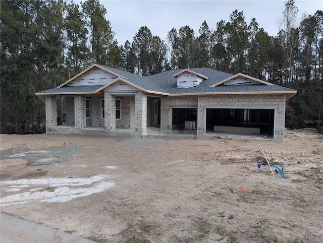 property under construction with dirt driveway, stone siding, roof with shingles, an attached garage, and a porch