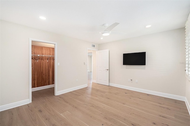 unfurnished bedroom featuring ceiling fan, light hardwood / wood-style floors, a walk in closet, and a closet