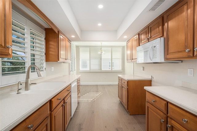 kitchen with white appliances, sink, decorative light fixtures, a chandelier, and light hardwood / wood-style floors