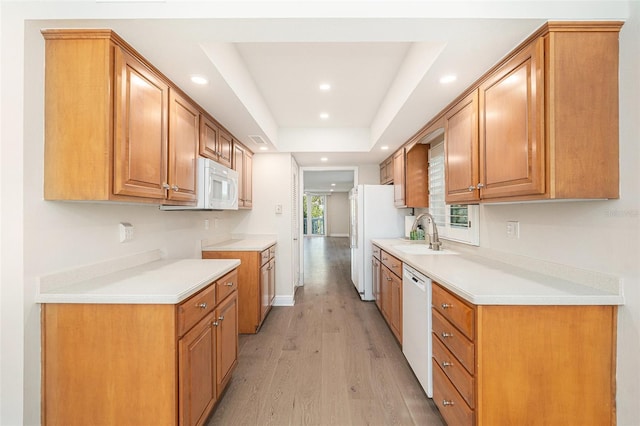 kitchen with a raised ceiling, white appliances, sink, and light wood-type flooring