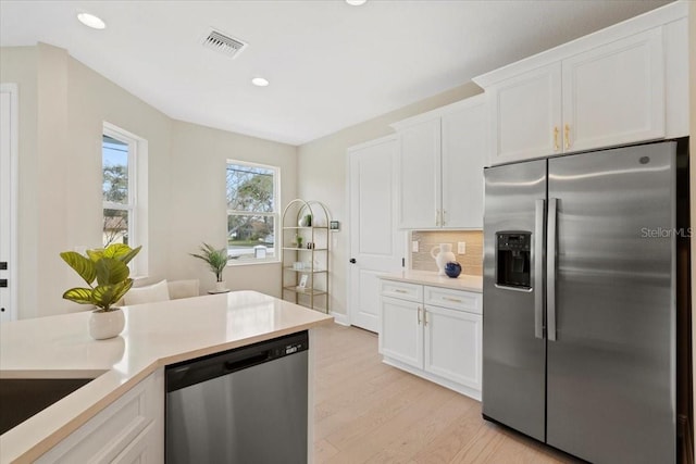 kitchen with tasteful backsplash, white cabinetry, light hardwood / wood-style flooring, and appliances with stainless steel finishes