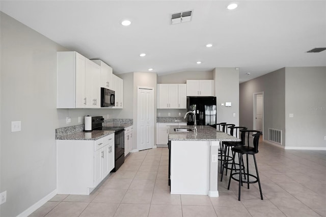 kitchen featuring light stone countertops, sink, black appliances, a center island with sink, and white cabinetry