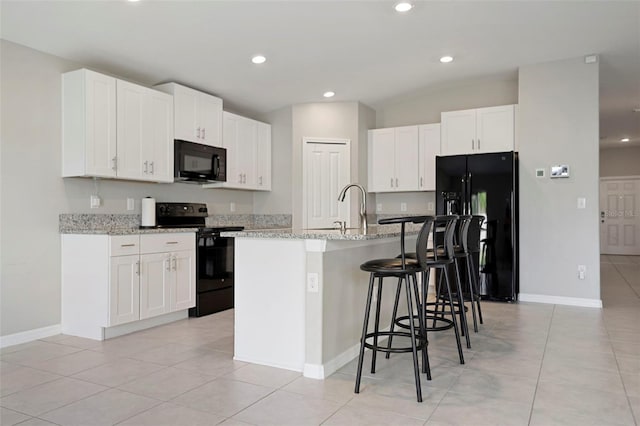 kitchen featuring light stone countertops, sink, a center island with sink, white cabinets, and black appliances