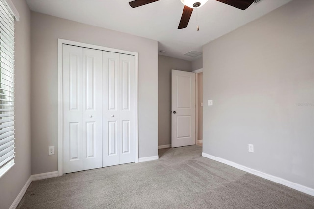 unfurnished bedroom featuring ceiling fan, multiple windows, light carpet, and a closet