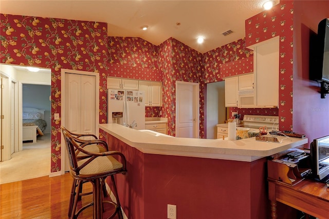 kitchen with white cabinetry, kitchen peninsula, light hardwood / wood-style floors, white appliances, and a breakfast bar