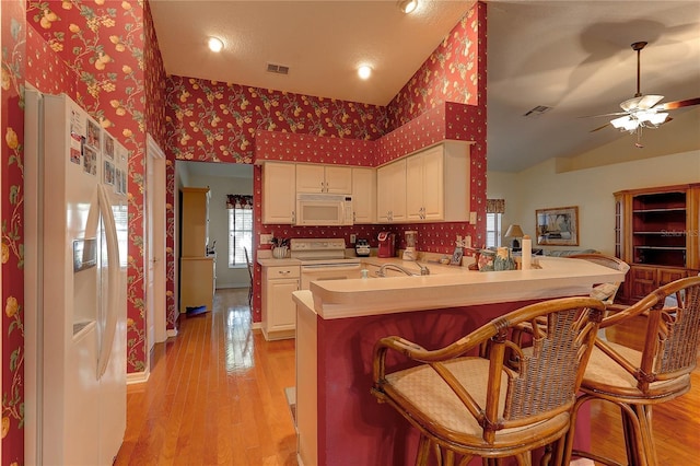 kitchen featuring a kitchen breakfast bar, light hardwood / wood-style flooring, kitchen peninsula, white appliances, and white cabinets