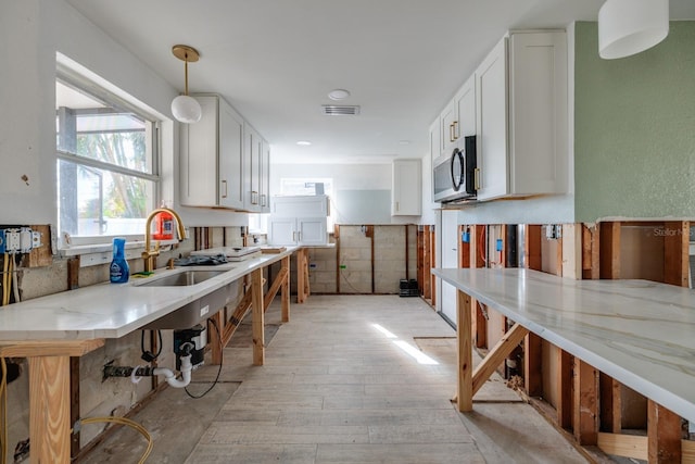 kitchen with white cabinets, light stone countertops, hanging light fixtures, and sink