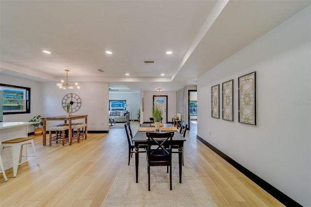 dining area with a chandelier, a raised ceiling, and light hardwood / wood-style flooring