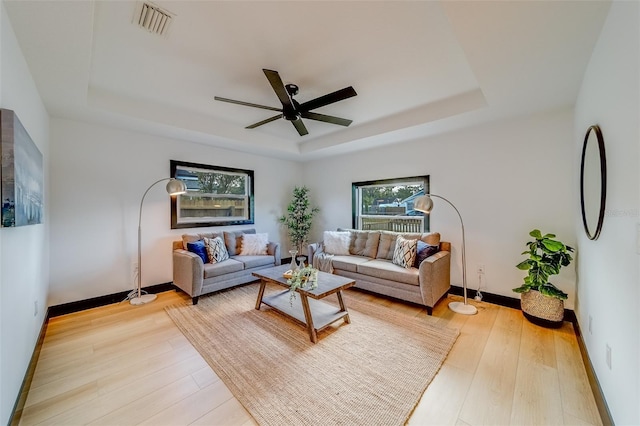 living room featuring ceiling fan, a raised ceiling, and light hardwood / wood-style flooring