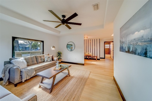 living room with ceiling fan, a raised ceiling, and light hardwood / wood-style flooring