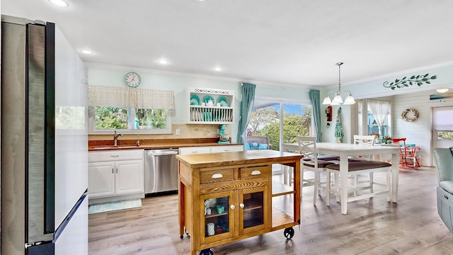 kitchen featuring appliances with stainless steel finishes, light wood-type flooring, sink, decorative light fixtures, and white cabinetry