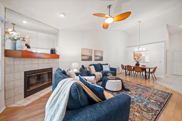 living room featuring a tile fireplace, ceiling fan, a textured ceiling, vaulted ceiling, and light wood-type flooring