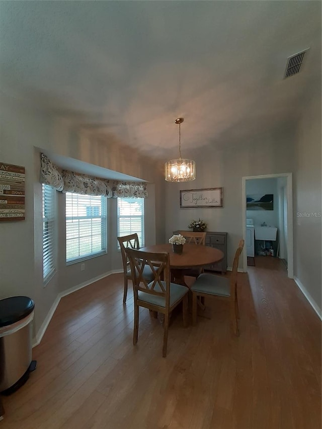 dining space with washer / dryer, wood-type flooring, sink, and a chandelier