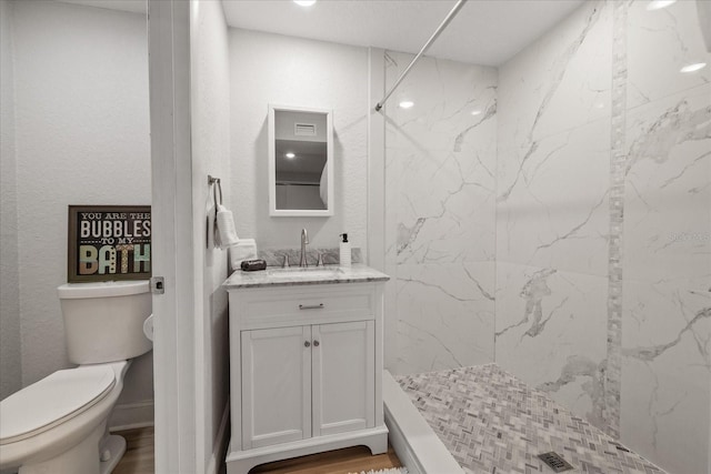 bathroom featuring a tile shower, vanity, wood-type flooring, and toilet