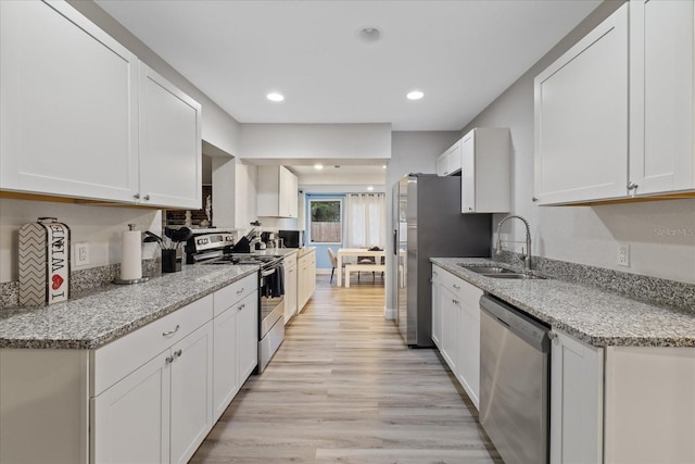 kitchen with sink, light stone counters, appliances with stainless steel finishes, white cabinets, and light wood-type flooring