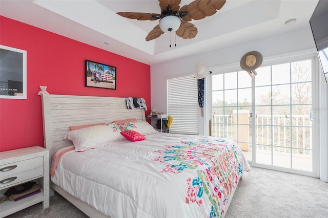 carpeted bedroom with ceiling fan, access to exterior, and a tray ceiling