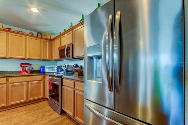 kitchen with dark stone counters, appliances with stainless steel finishes, and light hardwood / wood-style flooring